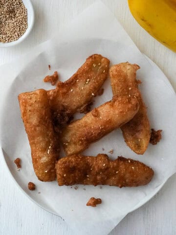 Five Thai Fried Bananas on a plate with some crispy bits of batter surrounding