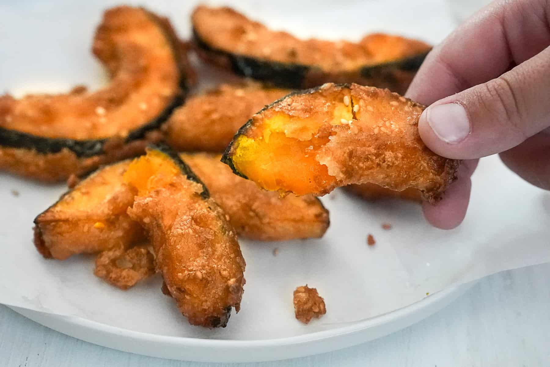 A hand holding a piece of Thai fried pumpkin