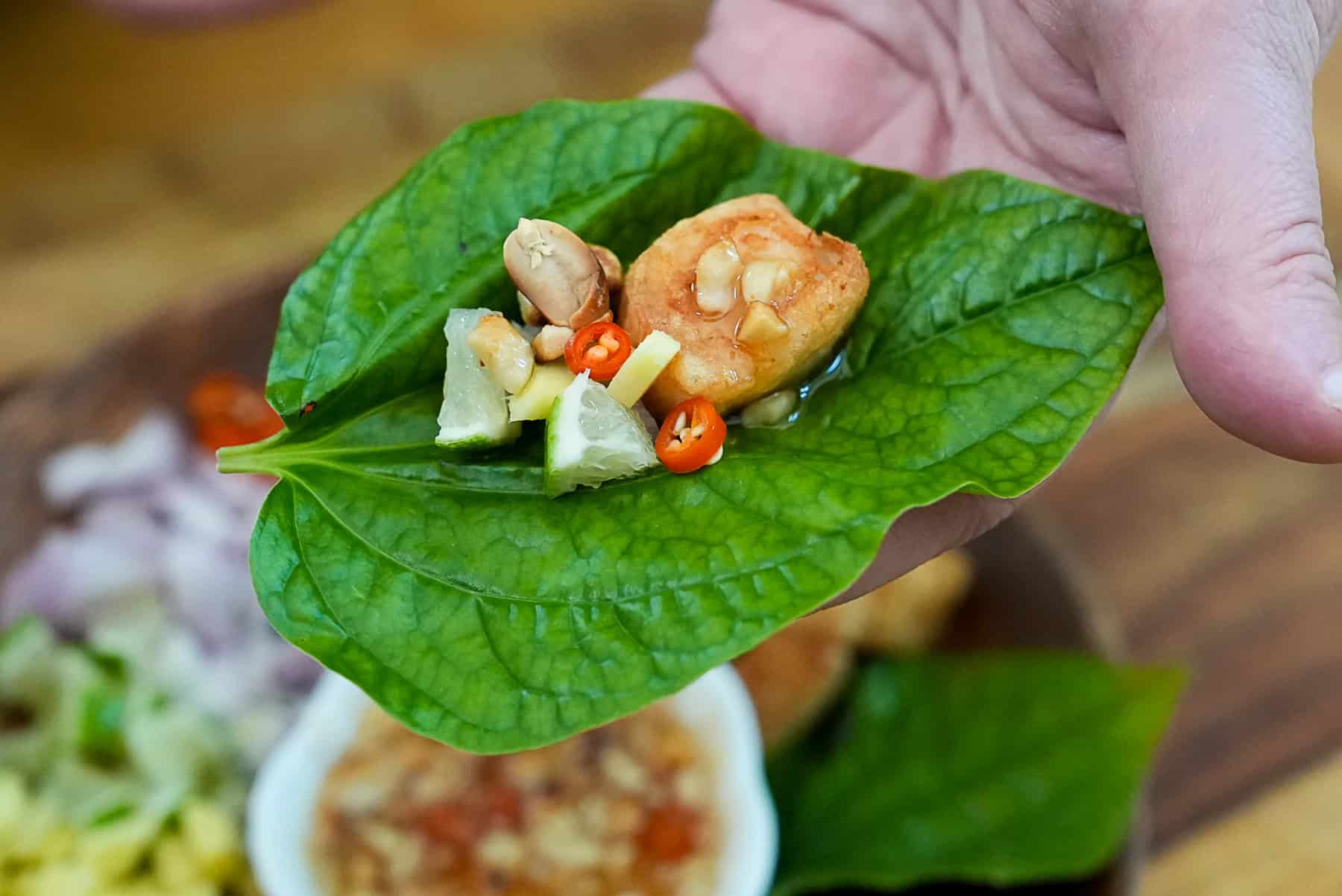 A wild pepper leaf with fried fish, peanuts, ginger, shallots, chilis, and lime