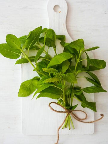 A bouquet of Thai holy basil stems tied with jute ribbon laying on a white cutting board