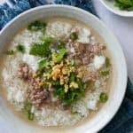 A bowl of Thai rice soup (Khao Tom) topped with minced pork, cilantro, green onions, and fried garlic