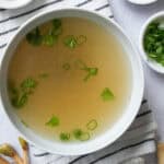 A bowl of Thai pork broth surrounded by Thai aromatic ingredients.